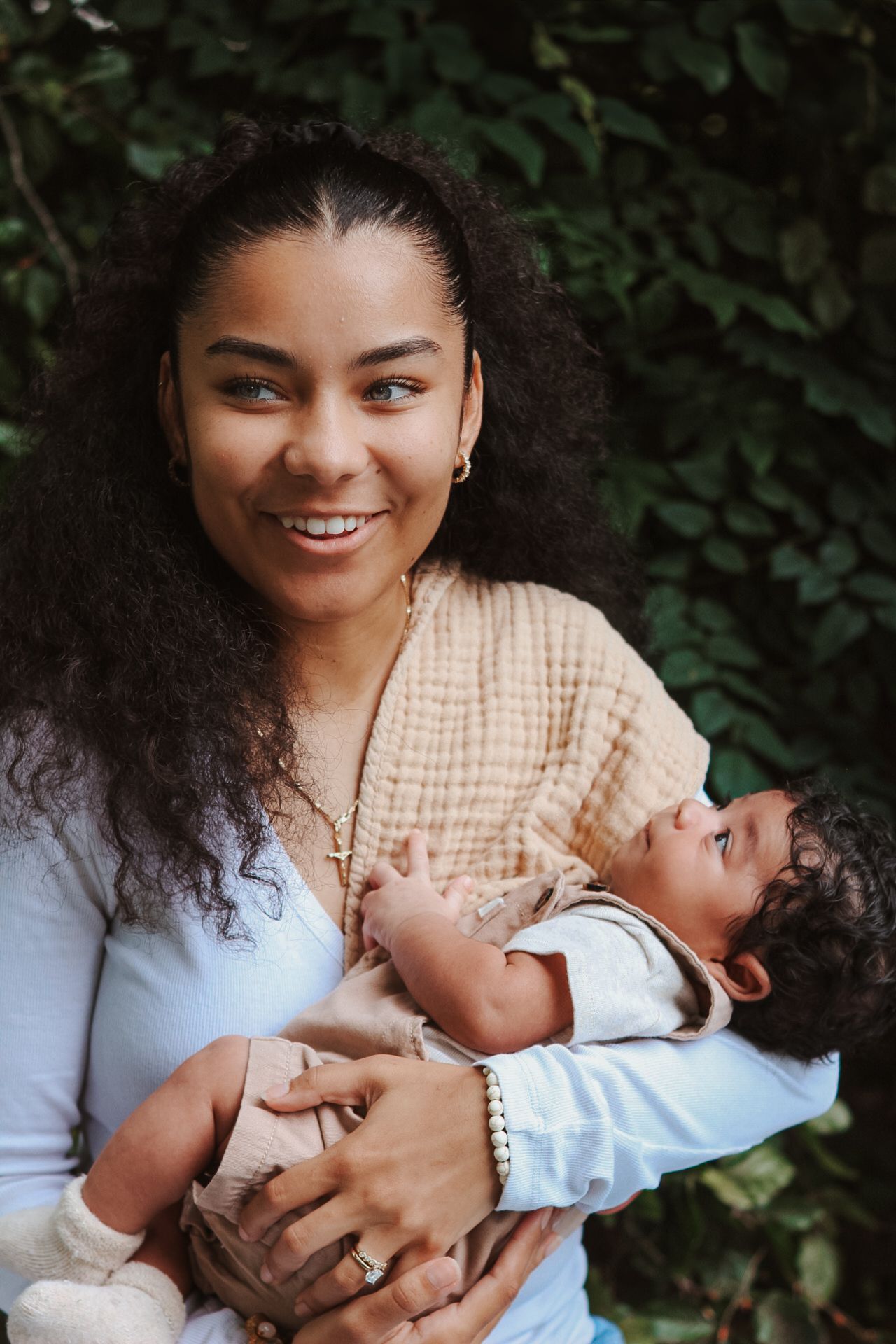 Parent in beige top sharing tender moments with baby against green foliage.