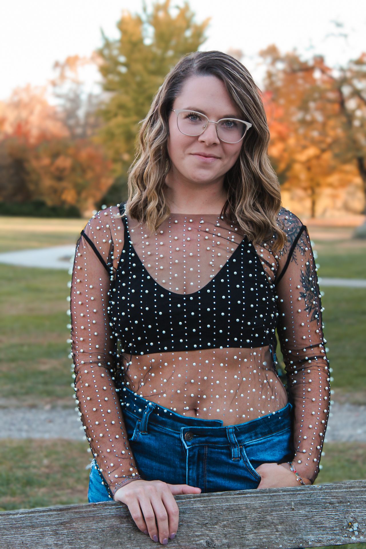 Casual autumn portrait showcasing a sheer polka dot top and denim against fall foliage.