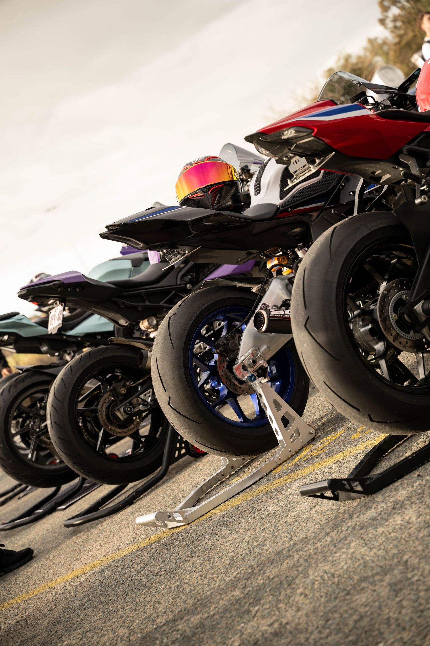 A row of sport motorcycles parked on stands at a racing track, showcasing colorful fairings and slick tires.