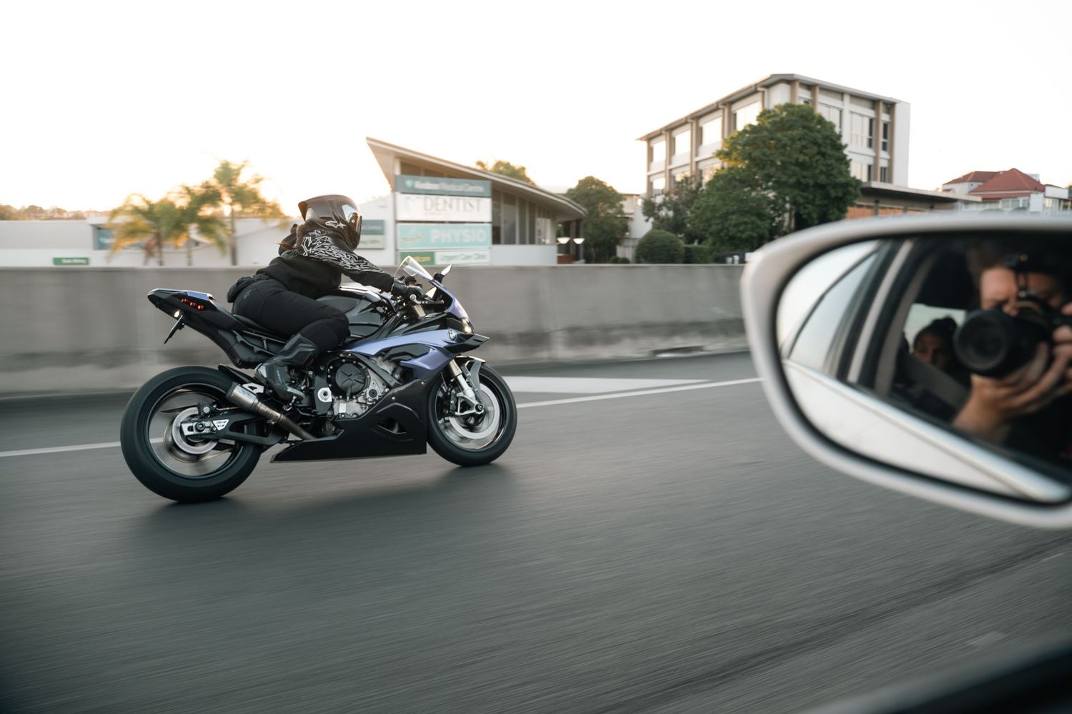 Motorcyclist riding a sport bike on a highway, captured from a car side mirror at sunset.