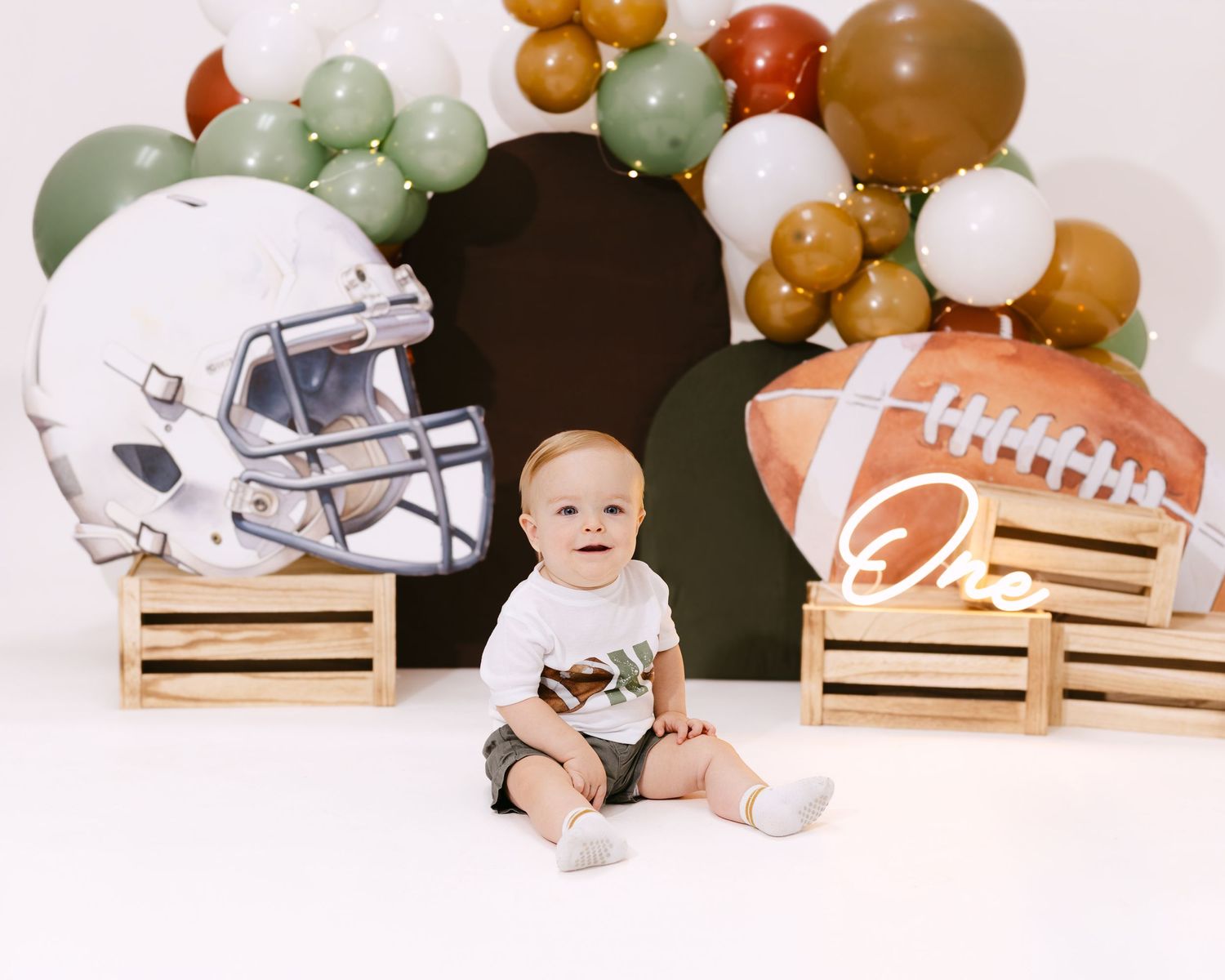 Baby's first birthday football themed photo shoot with helmet, balloons, and a football on wooden crates.
