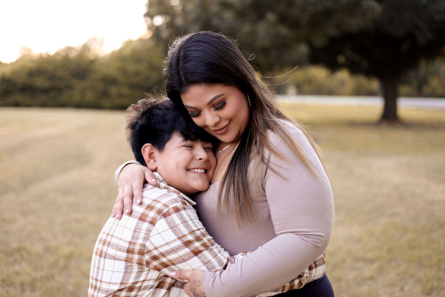 A woman warmly embraces an older boy in a sunlit park, sharing a tender and loving hug outdoors.