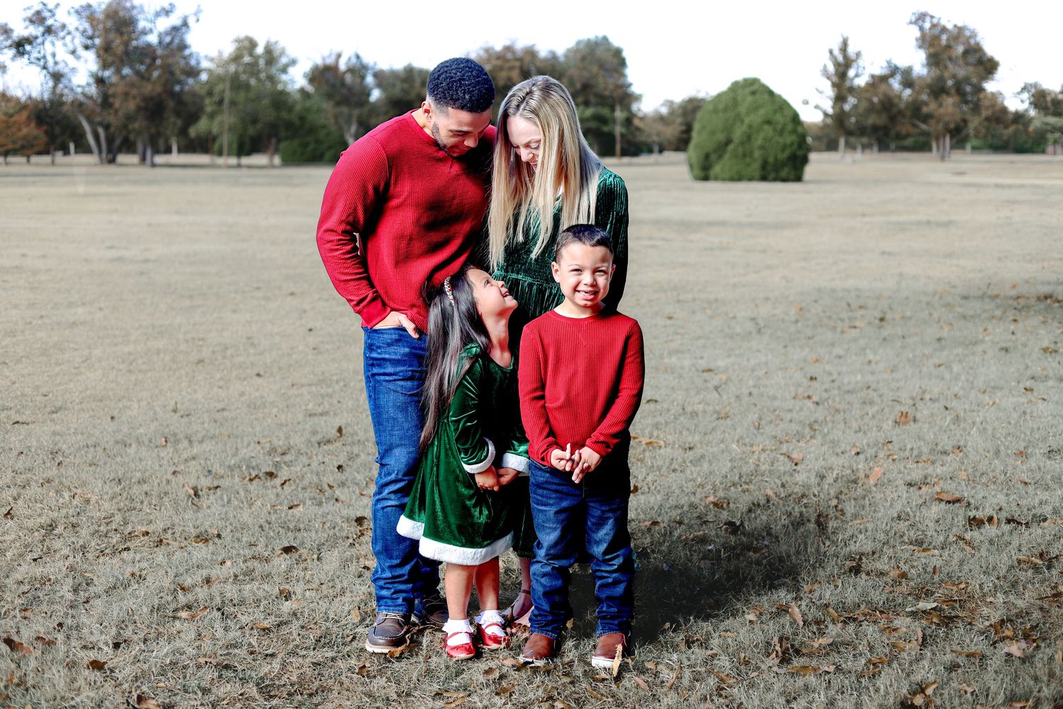 Family members in casual clothing pose together on grass under autumn trees.