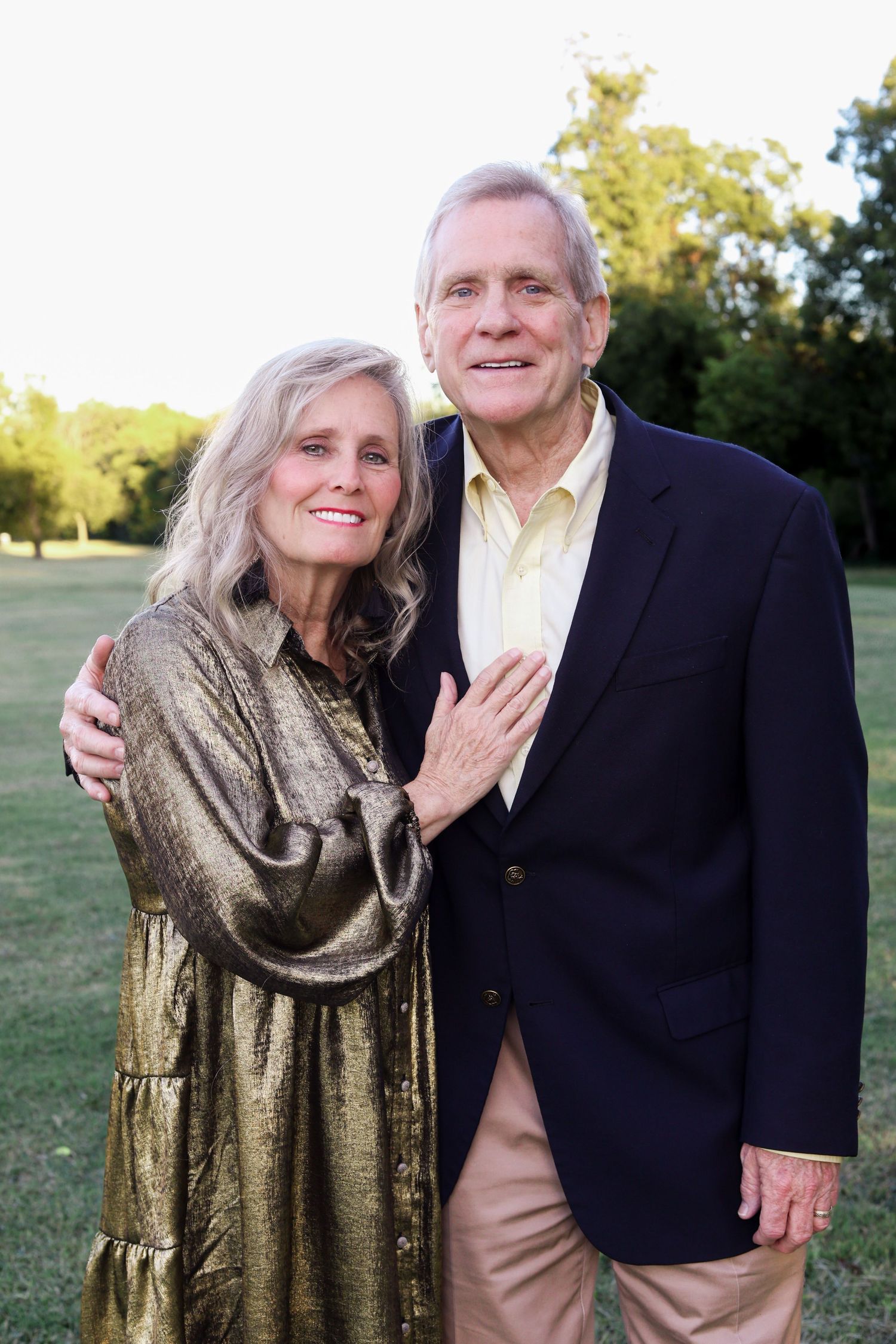 Smiling older couple posing outdoors in elegant attire at golden hour in a green park.