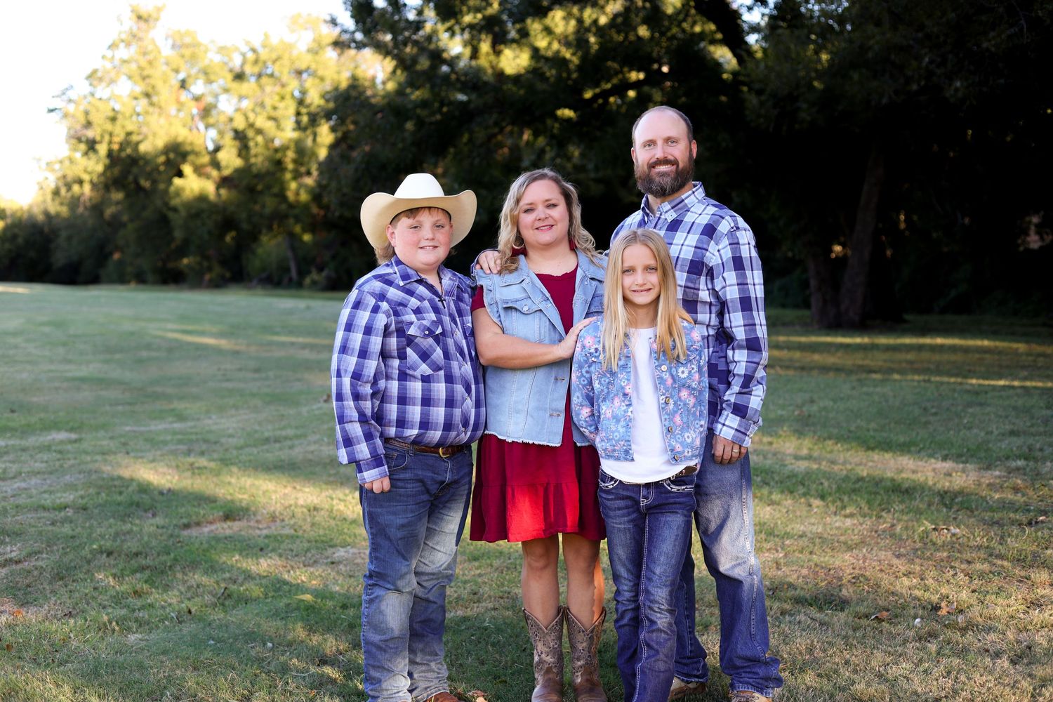 Family of four in western attire posing outdoors with cowboy hats and plaid shirts.