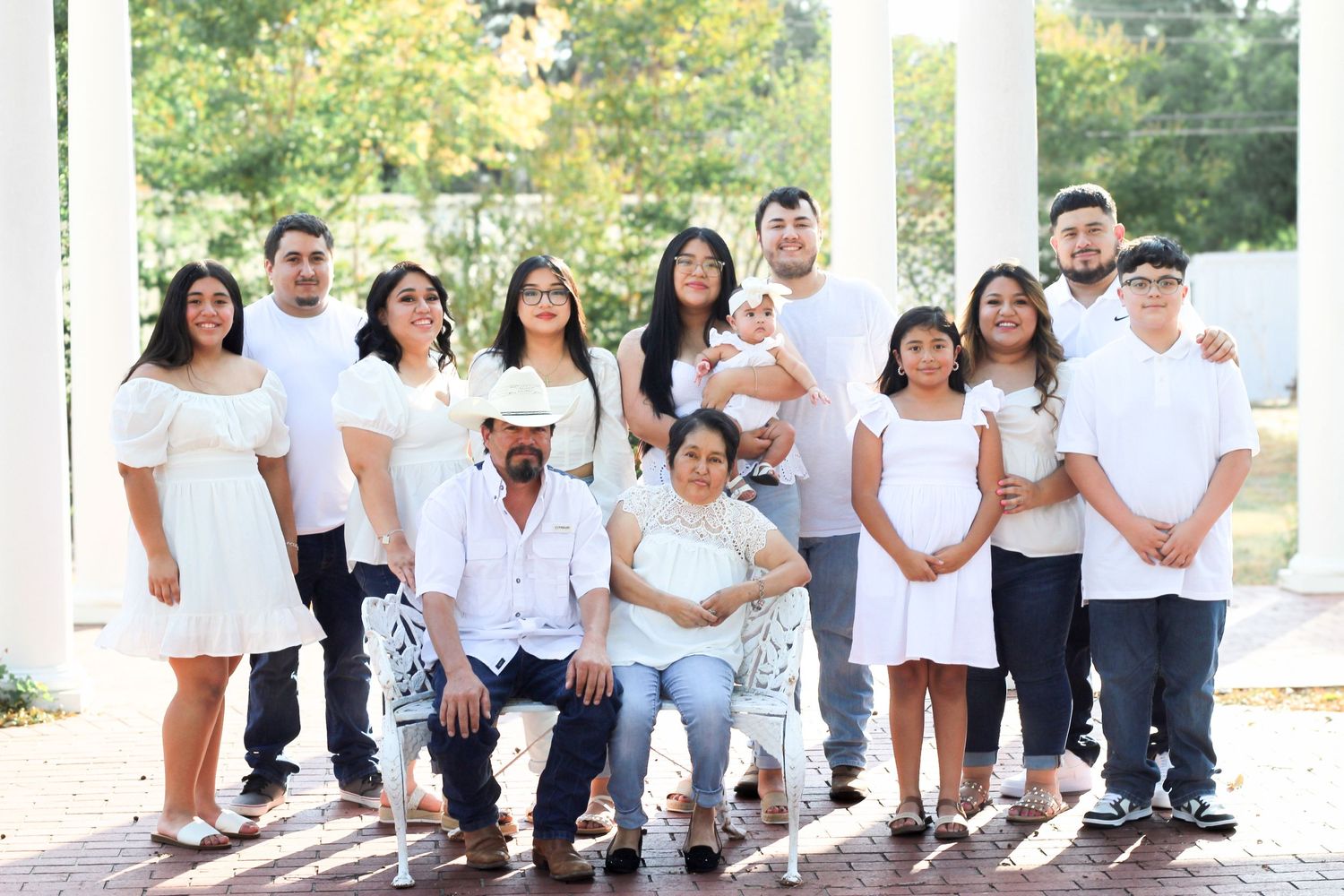 Large Latino family posing together in matching white outfits for a formal outdoor portrait photo.
