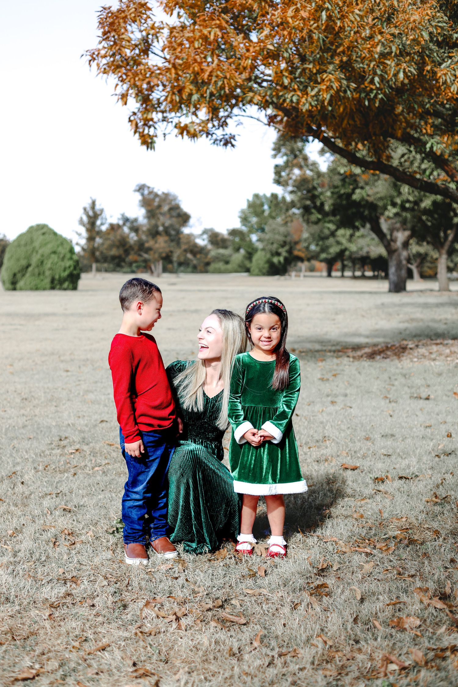 Family members in festive attire interact playfully on grass under autumn trees.