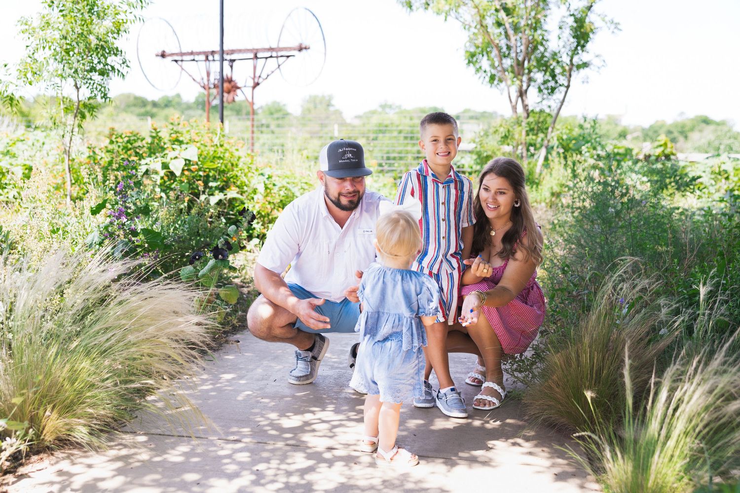 A family of four enjoys a sunny day together on a garden path.