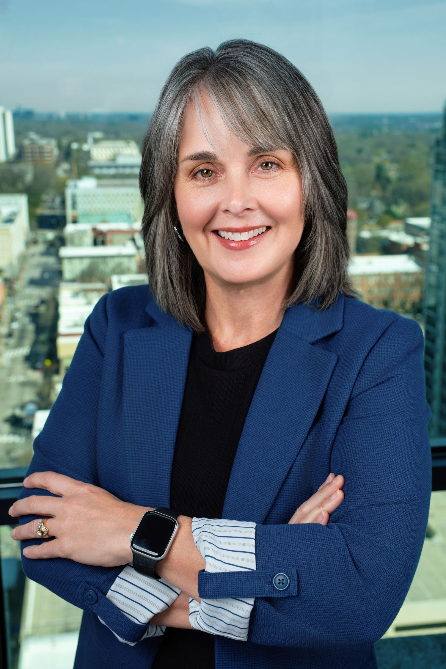 Professional portrait of person in navy blazer with smart watch against city view.
