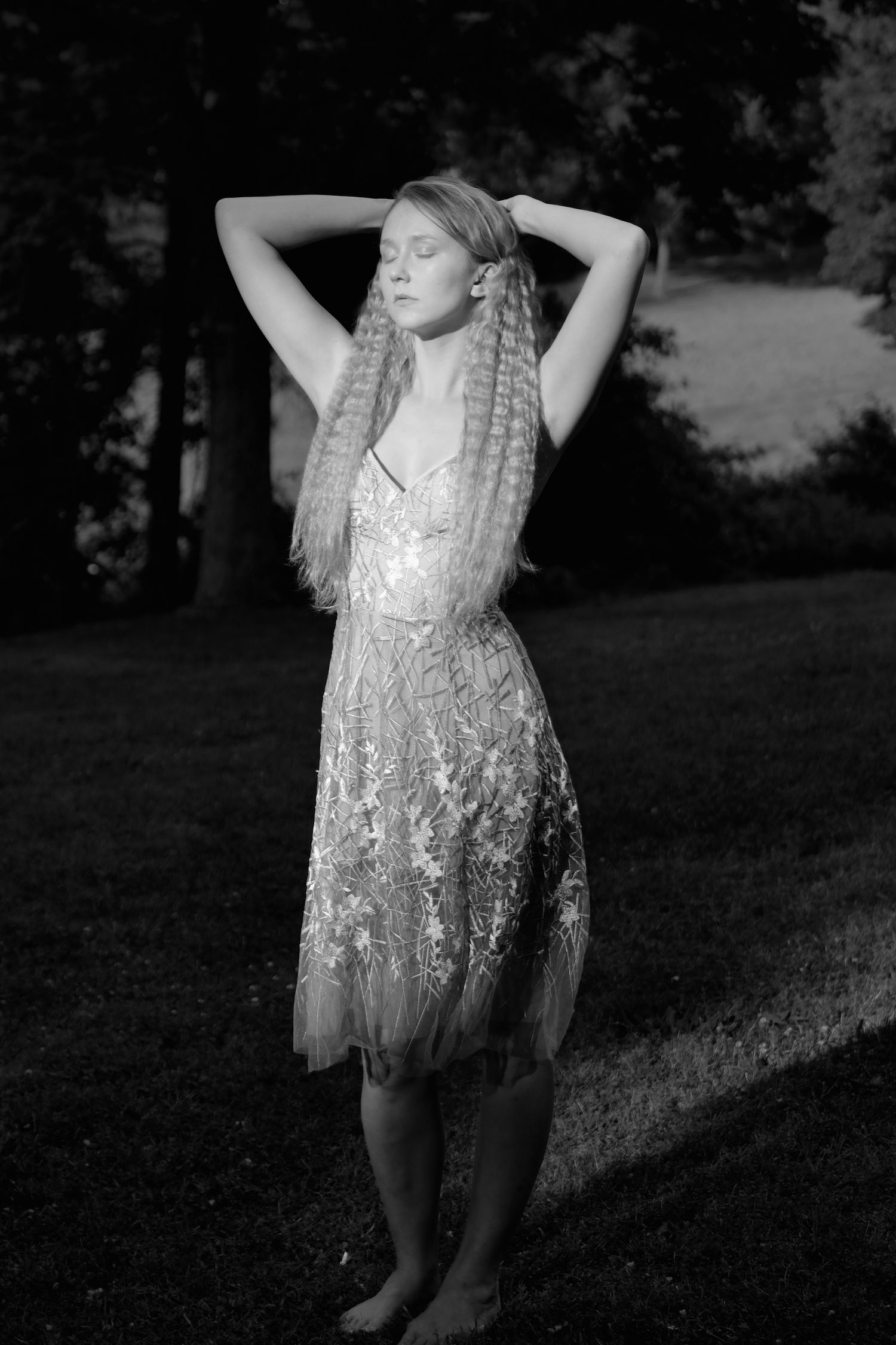 Black and white portrait of someone in a lace dress posing outdoors.