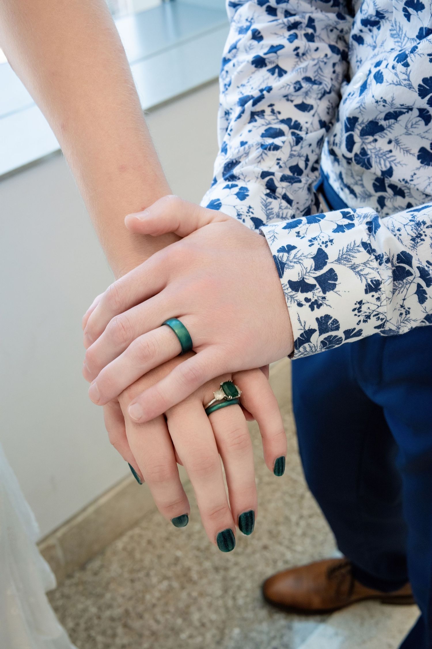Close-up of two hands wearing matching teal silicone wedding bands with a floral print shirt visible.