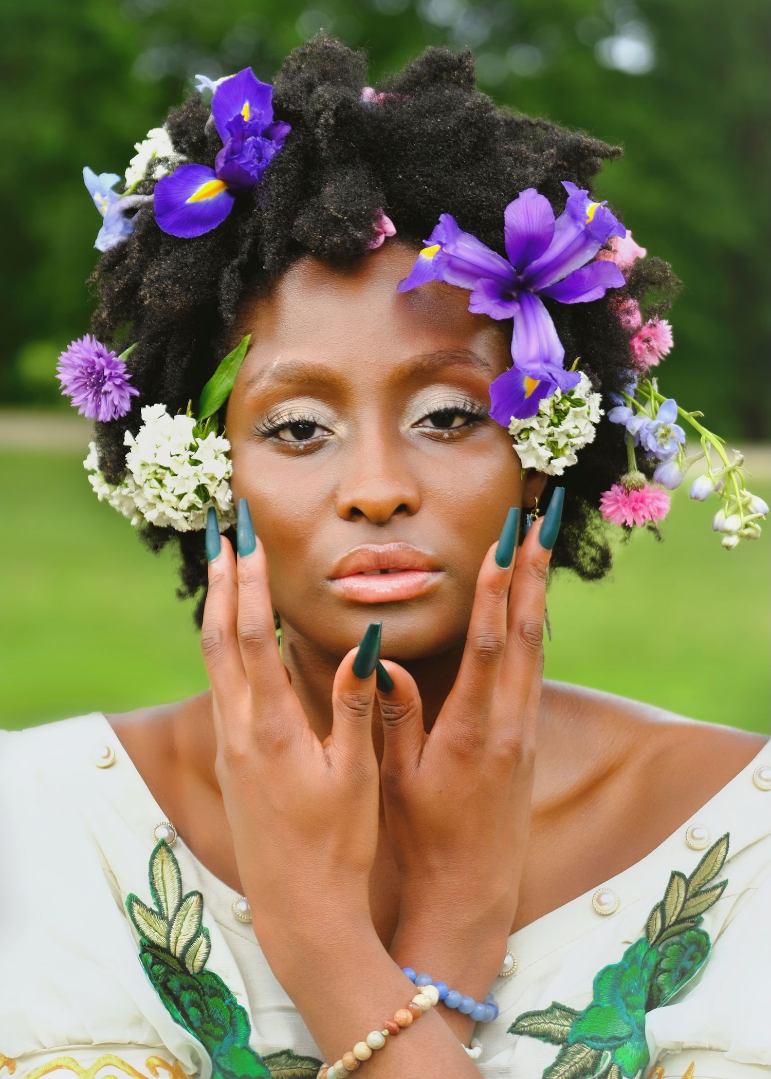 Portrait with purple flowers adorning natural hair against green background.