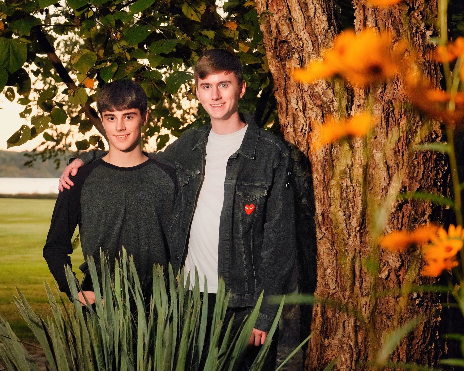 Two people standing together outdoors with autumn colors in the background.