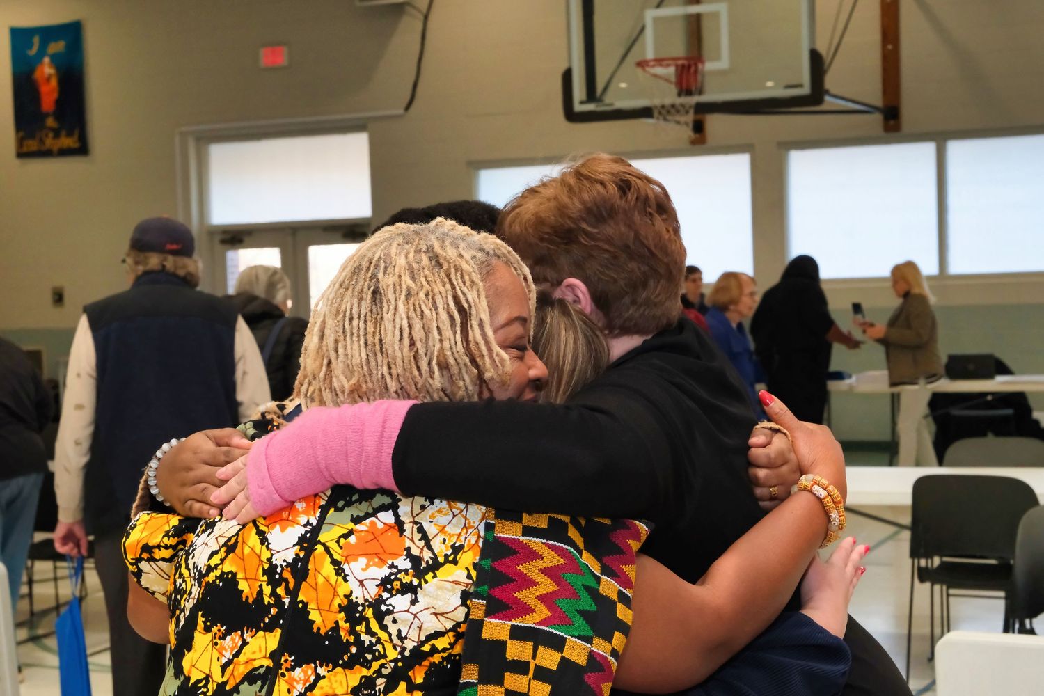 People embrace in a group hug during a community gathering in a gymnasium setting.