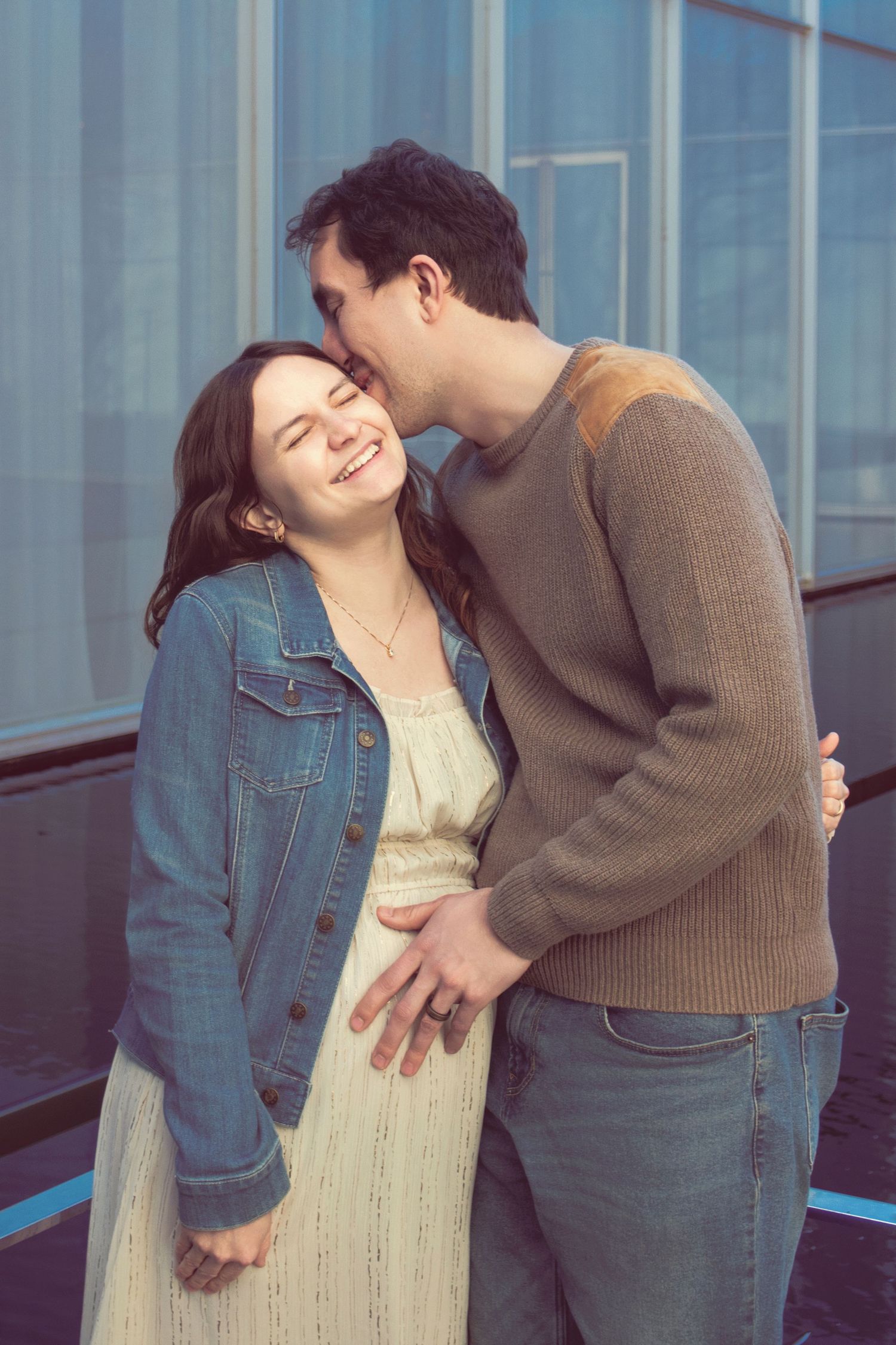 A couple sharing a romantic moment against a modern glass building background with natural light.