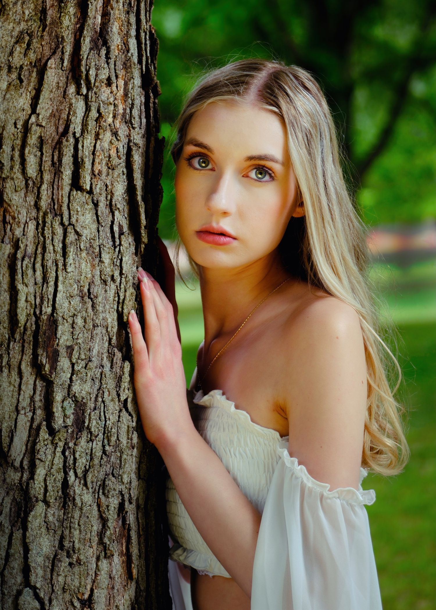 Natural light portrait by tree trunk with off-shoulder white top.
