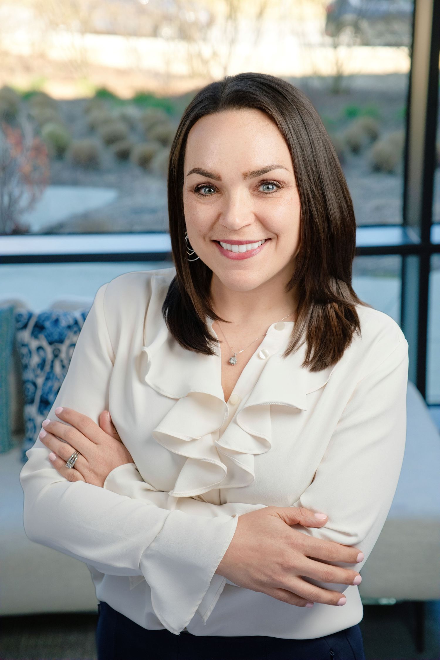 Professional business portrait of someone in a white ruffled blouse smiling warmly against an interior background.