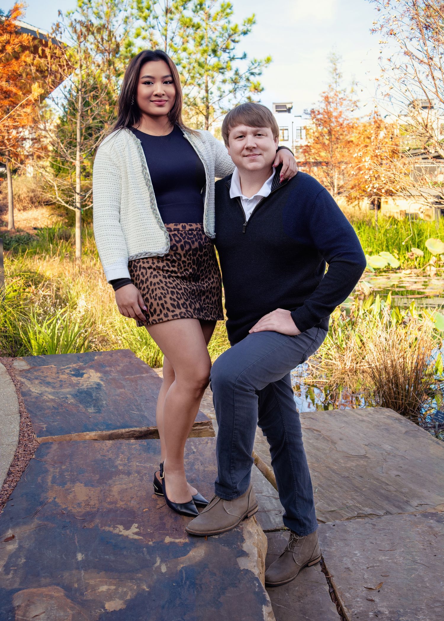 A couple poses together on a rocky outdoor path surrounded by autumn foliage and greenery.