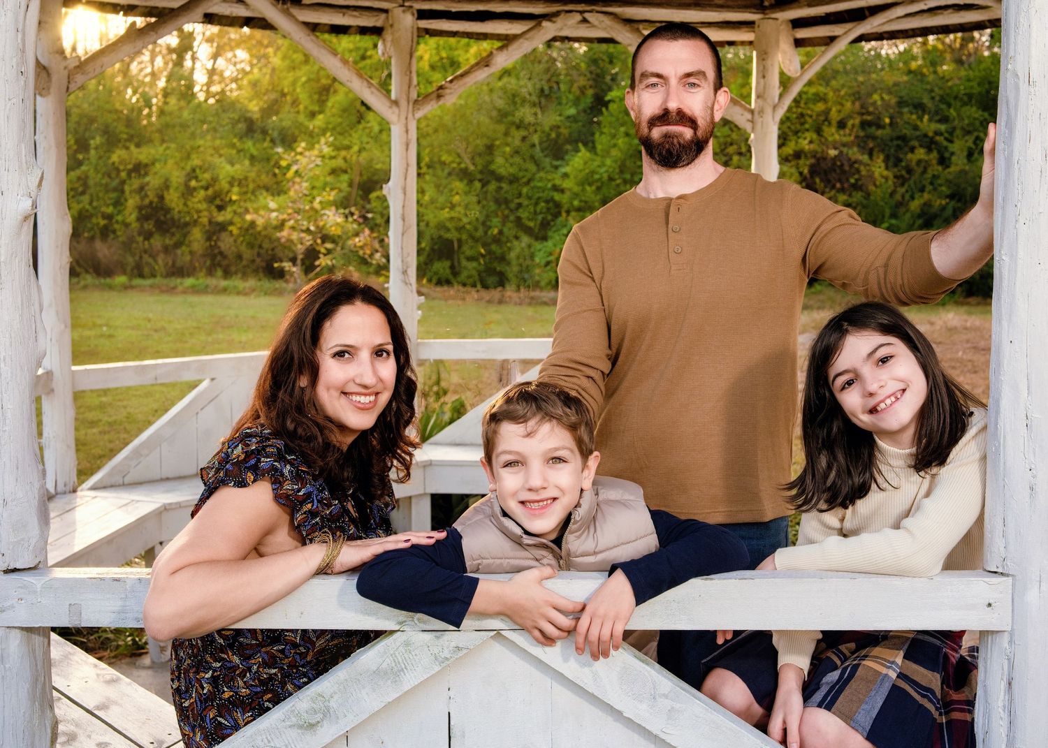 A family poses together in a rustic wooden gazebo on a sunny day.