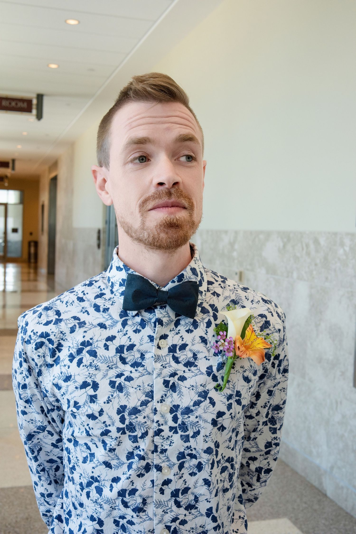 A person wearing a blue and white floral print shirt and bowtie with a yellow boutonniere.