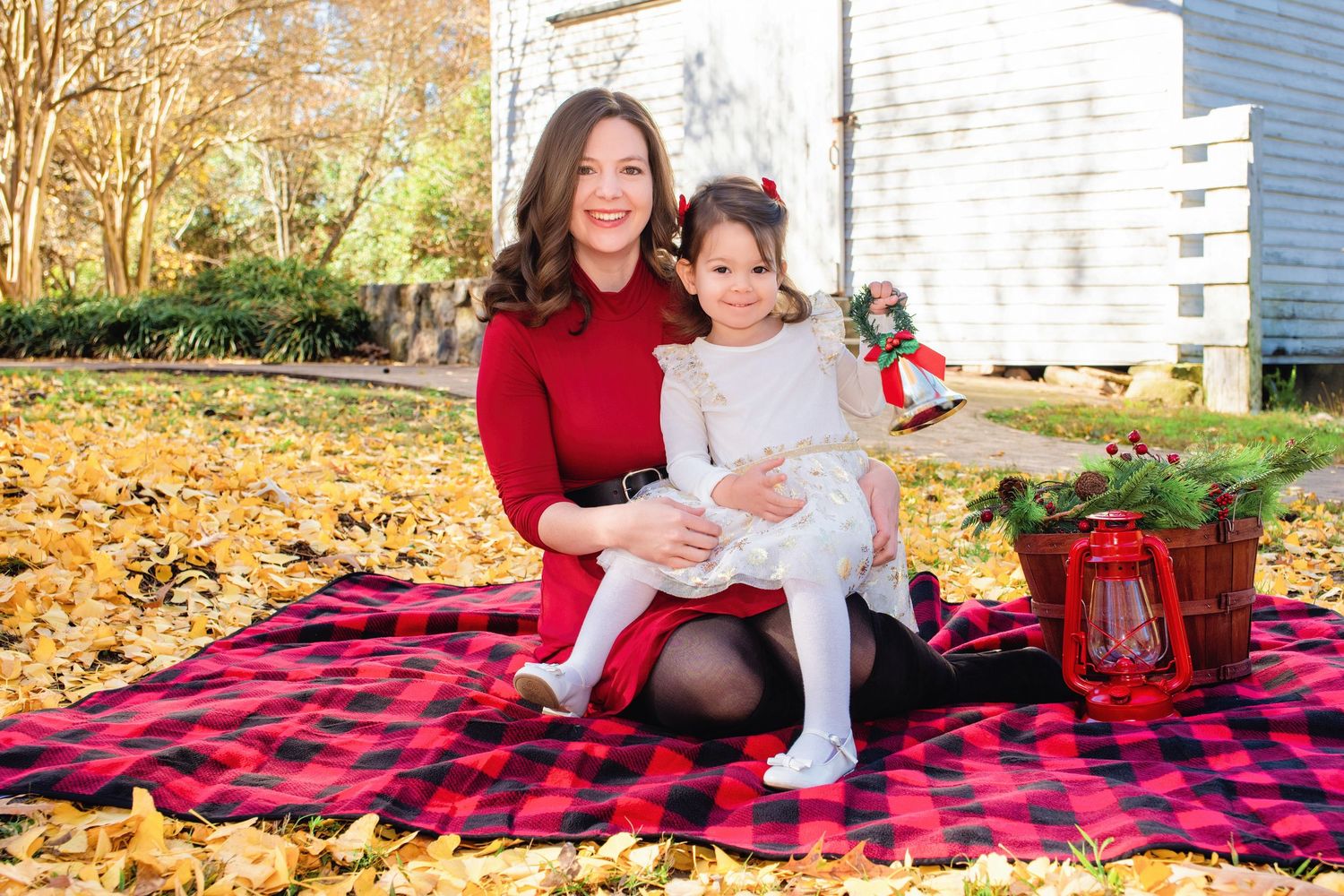 People sitting on a red and black plaid blanket surrounded by autumn leaves during an outdoor photo session.
