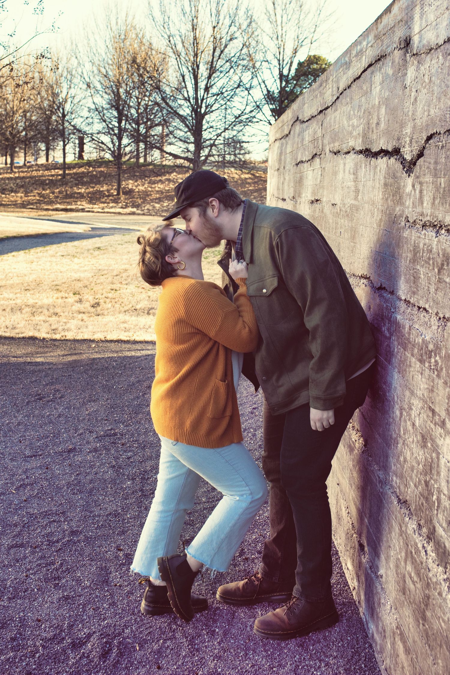 A romantic couple shares a tender moment against a concrete wall on a winter afternoon at a park.