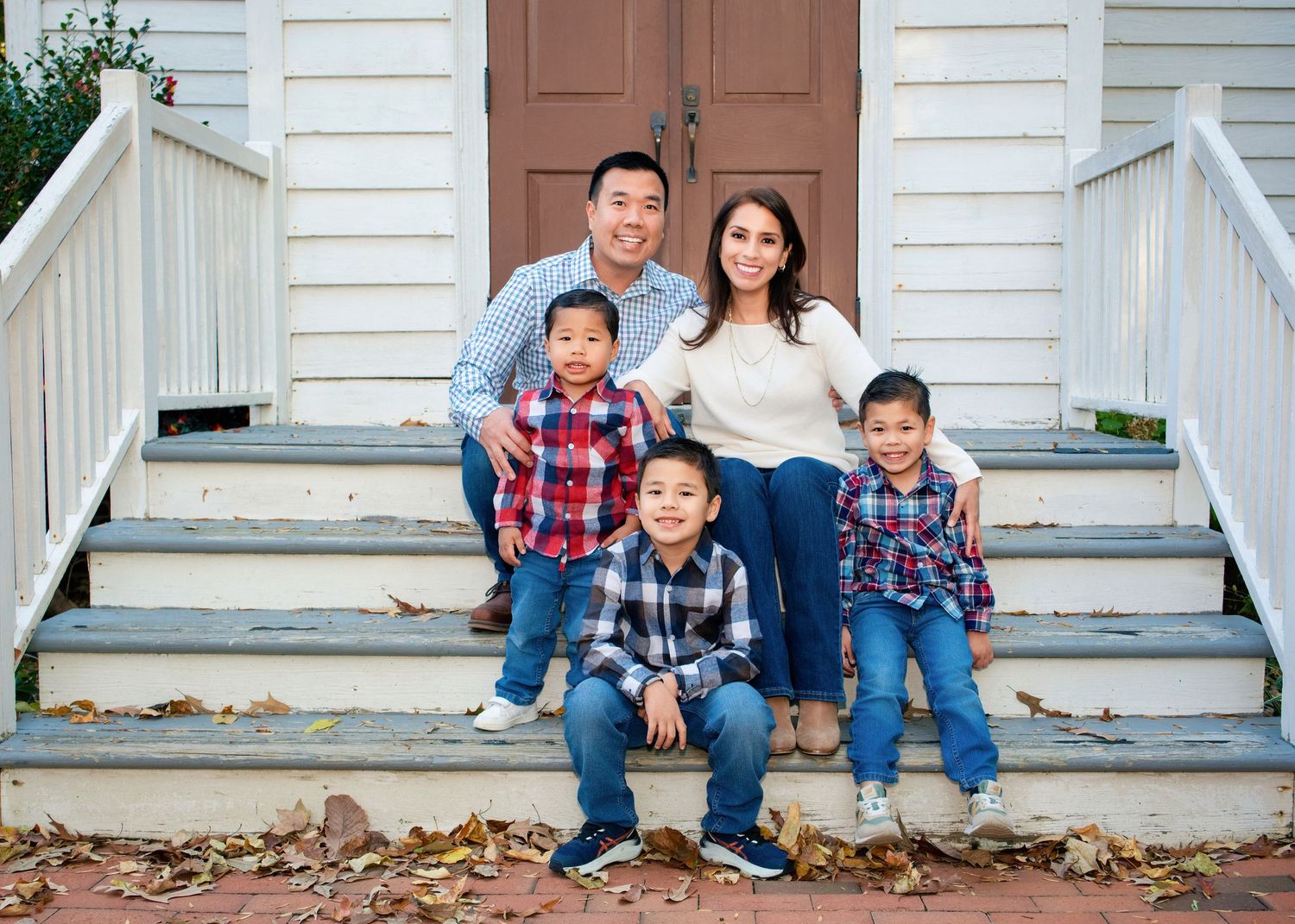 Family sitting on white porch steps of house in autumn with fallen leaves scattered around.