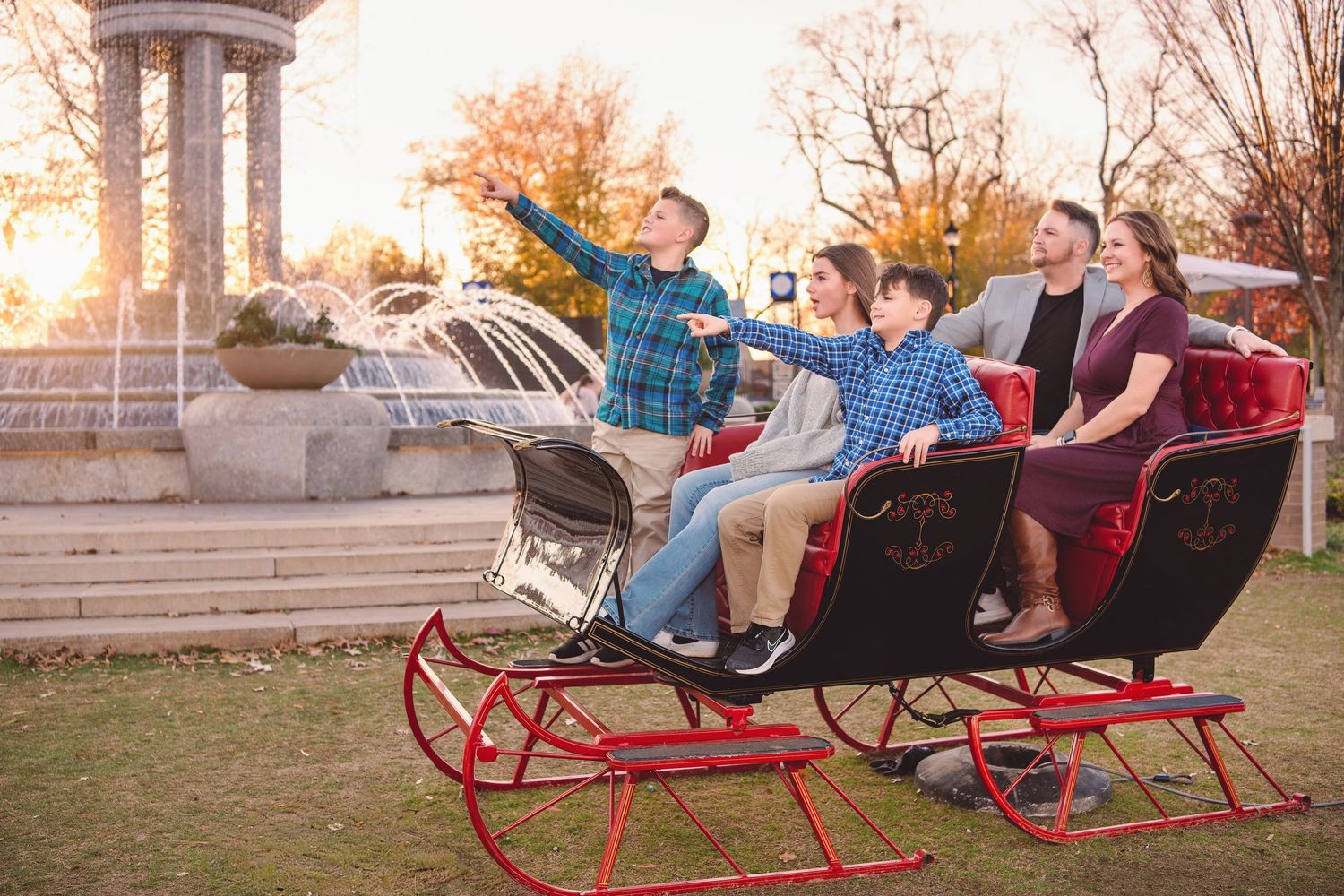 Family of four sits in large red sleigh during outdoor holiday photo session at sunset.