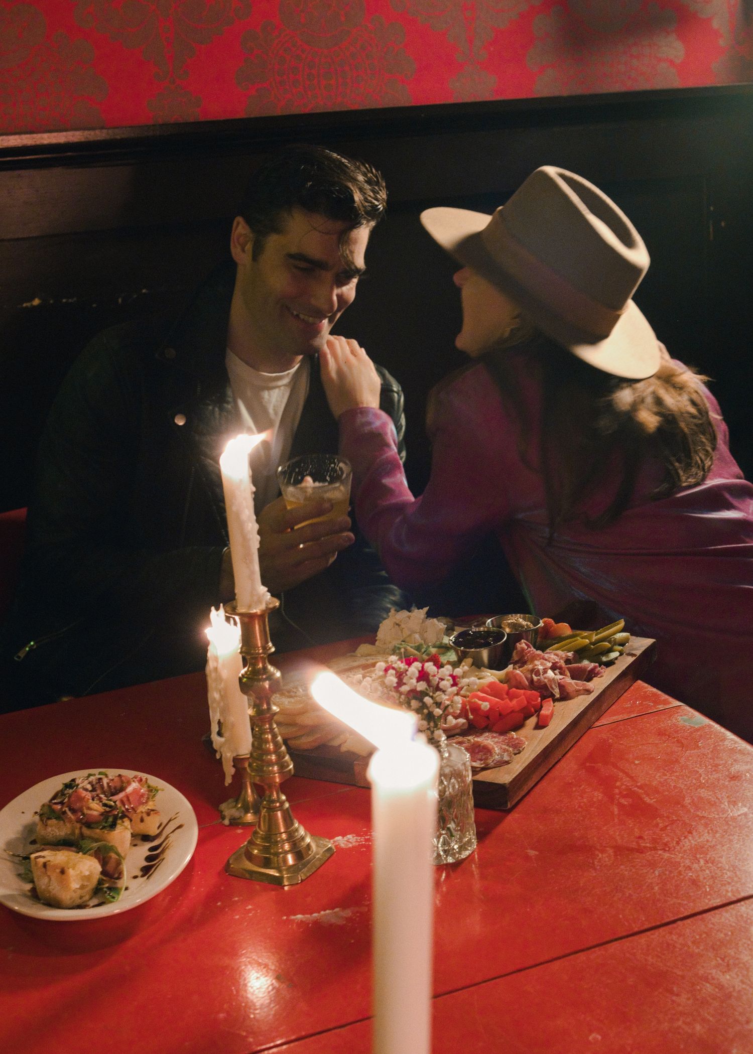 Romantic candlelit dinner scene with food and drinks on a red table.