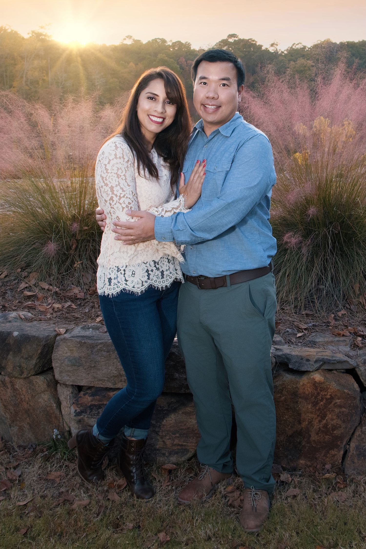 A couple stands together at sunset with ornamental grasses and rocks in the background.
