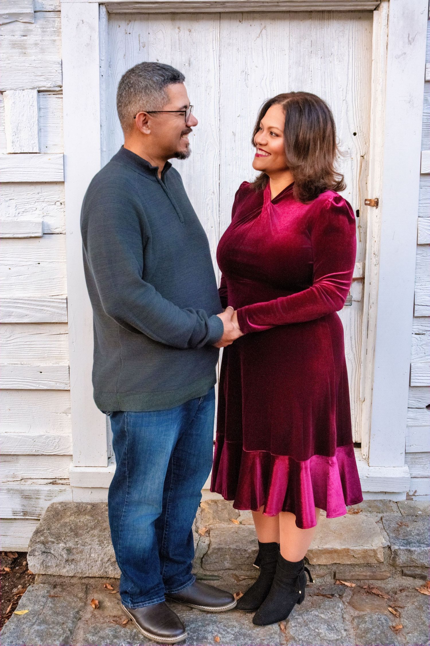A couple shares an intimate moment while standing against a white wooden wall.