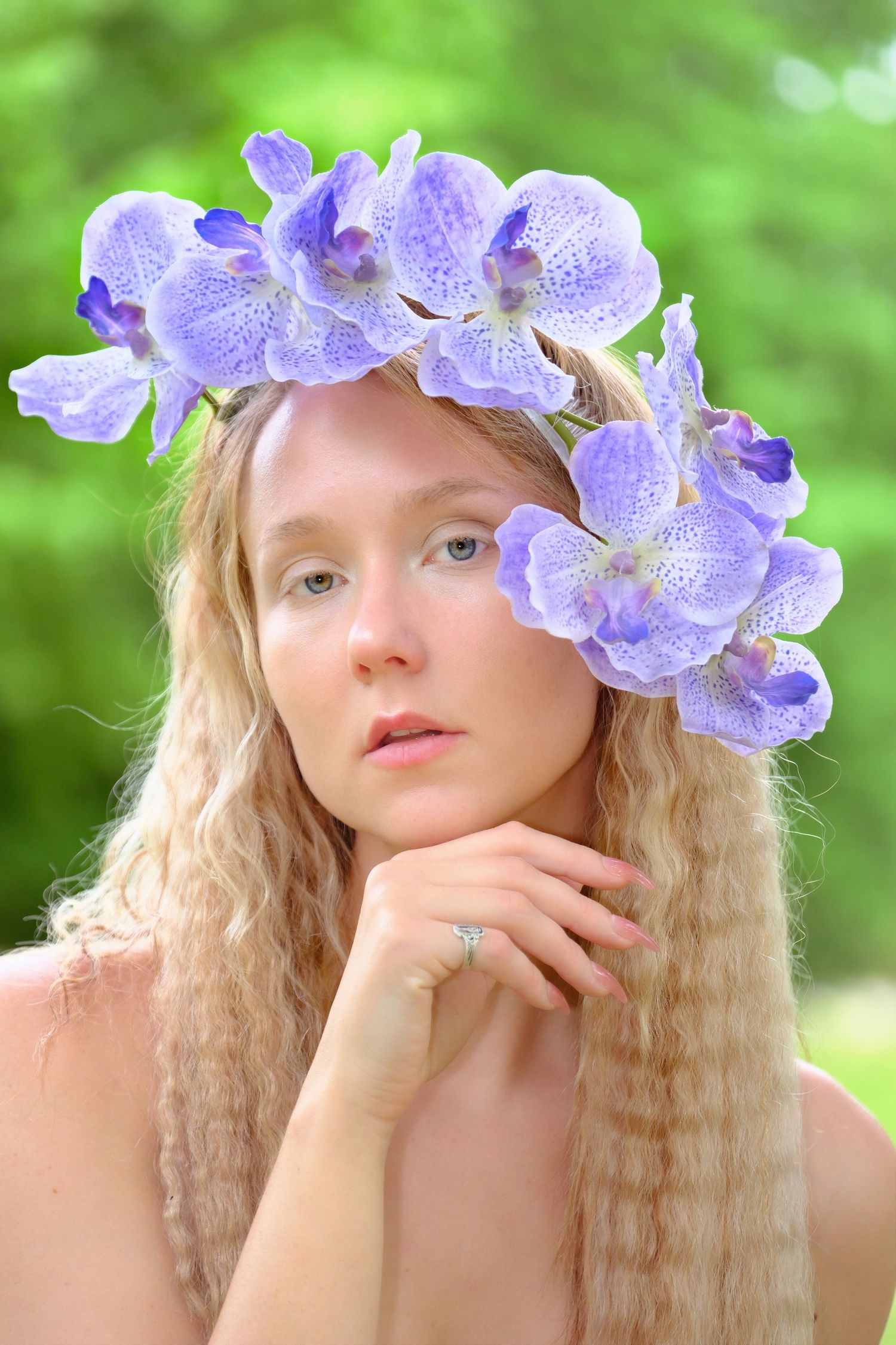 Ethereal portrait with purple orchid crown against soft green background.
