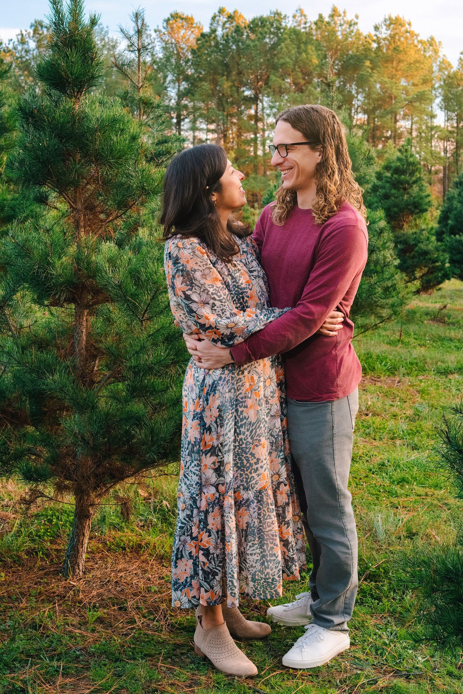 A couple embraces while standing among pine trees during golden hour.