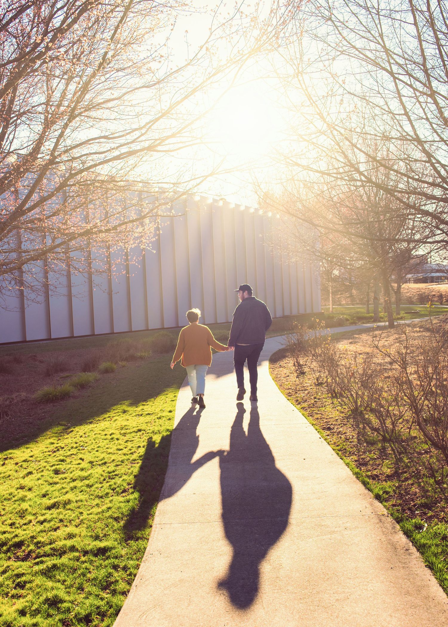 Two people walk along a sunlit path with long shadows cast behind them on a bright autumn afternoon.