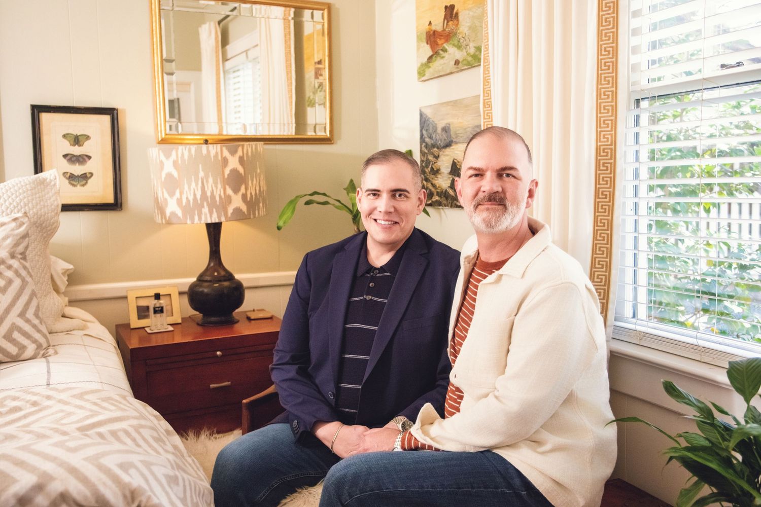 Two people sit together on a sofa in a cozy living room with decorative accents and natural lighting.