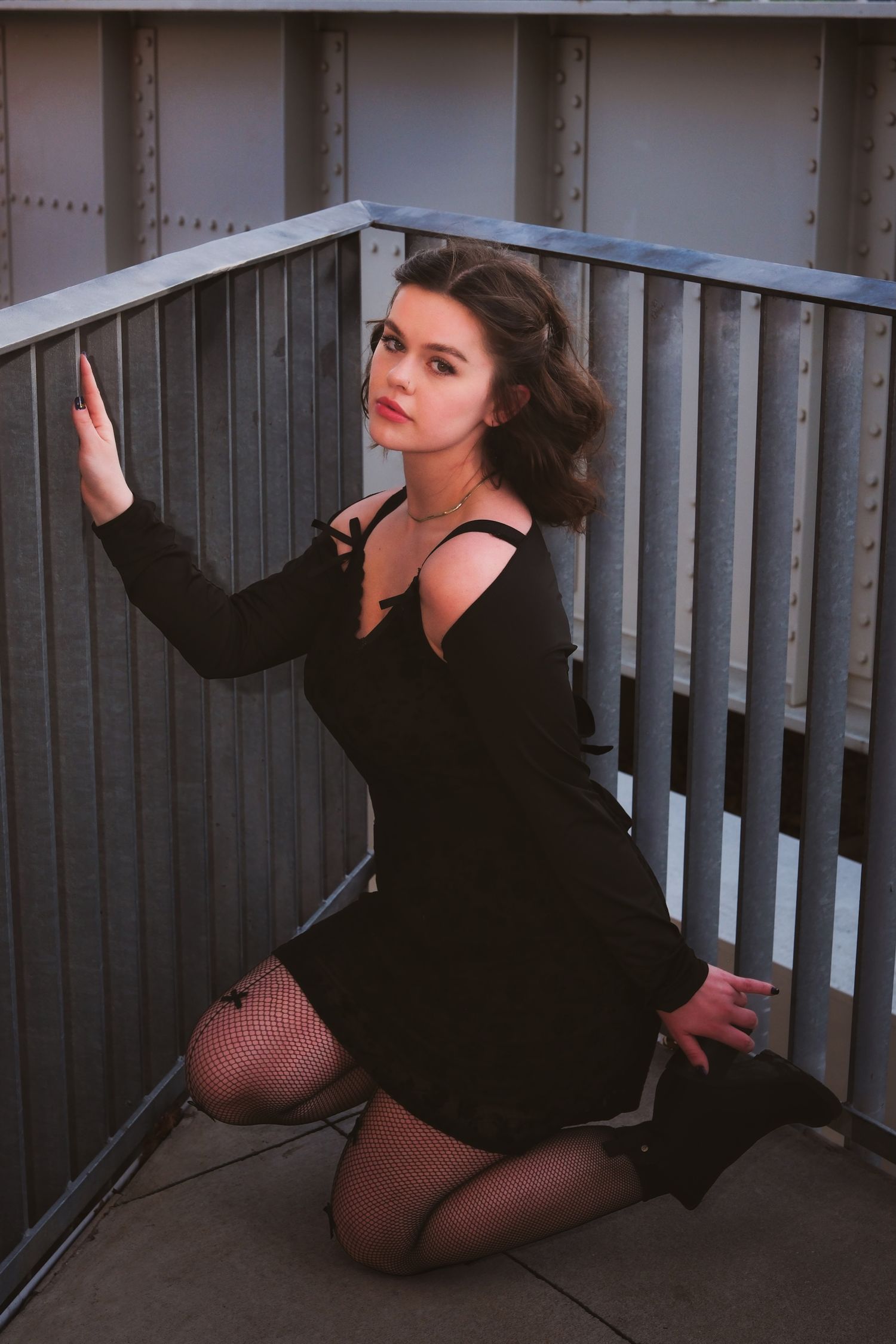 Dramatic portrait in black dress on balcony with moody lighting and urban backdrop.