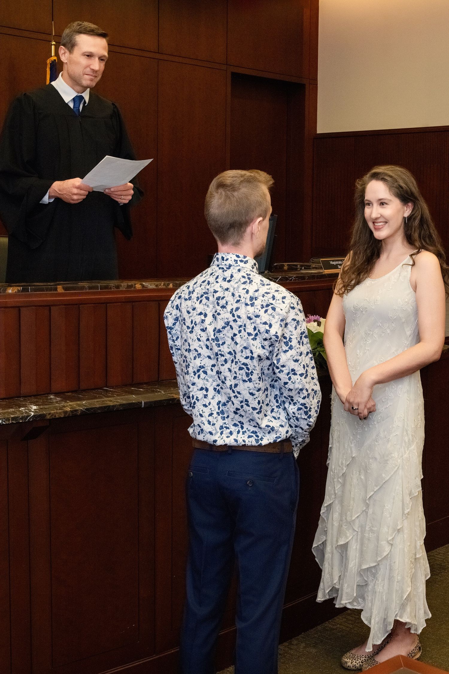 A couple exchanges vows during an indoor wedding ceremony with an officiant in a black robe standing at a wooden podium.