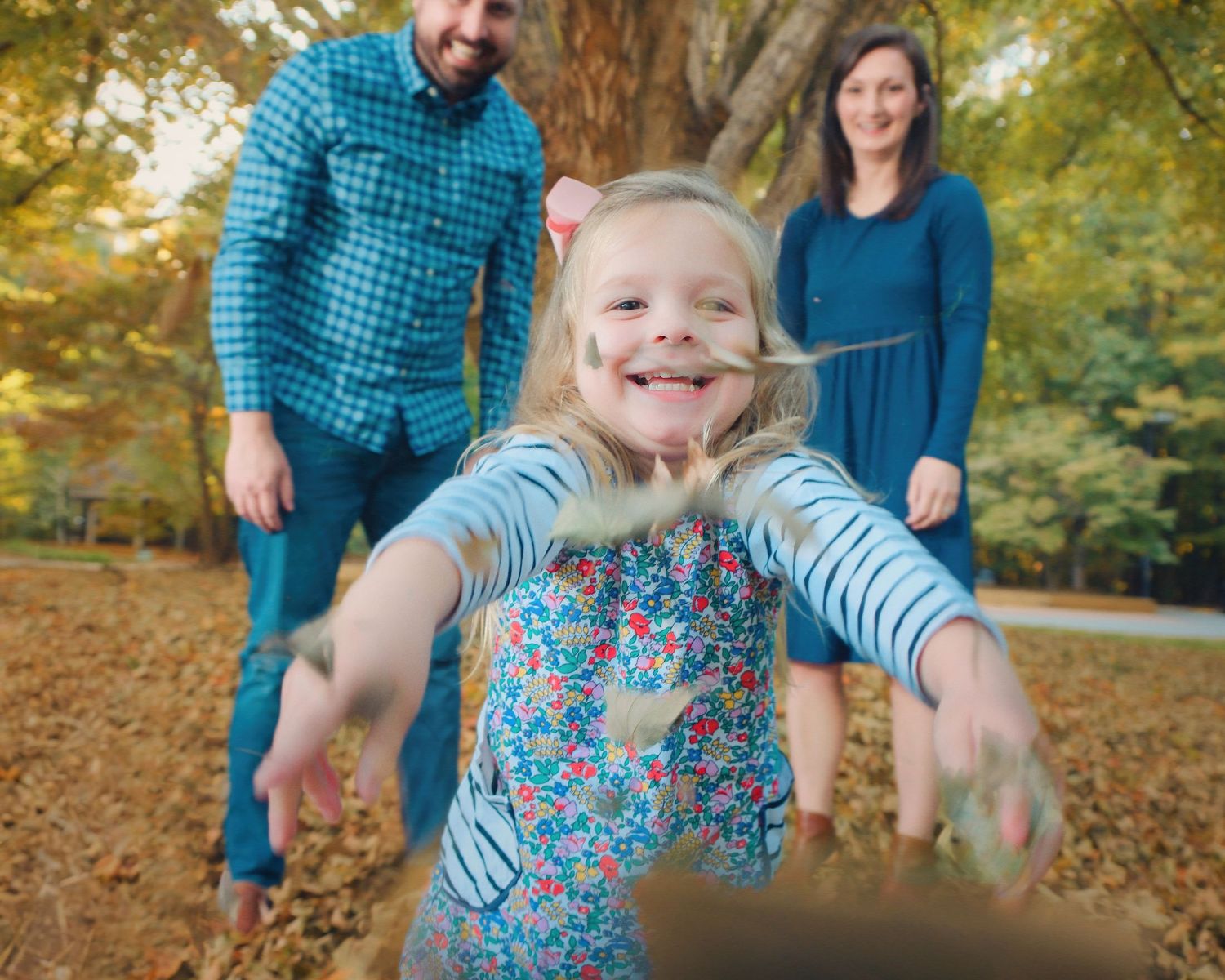 Candid autumn family photo with child jumping joyfully in foreground.