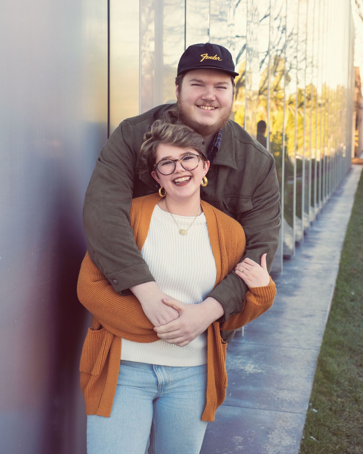 A couple sharing a romantic moment along a tree-lined pathway during golden hour sunset.