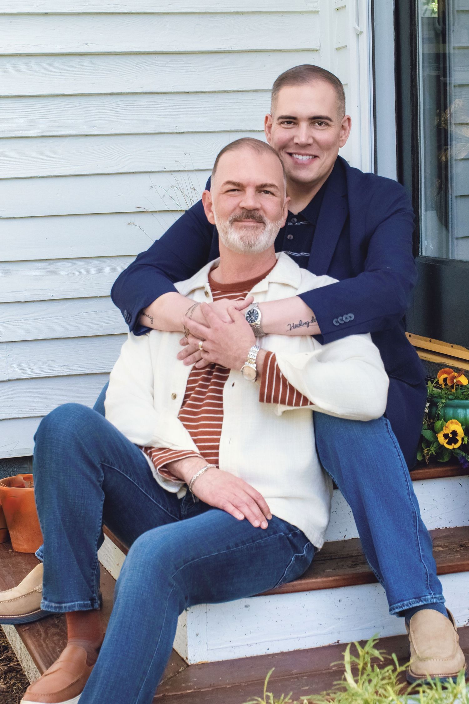 A couple sits together on porch steps, wearing coordinating navy and white outfits in a casual embrace.