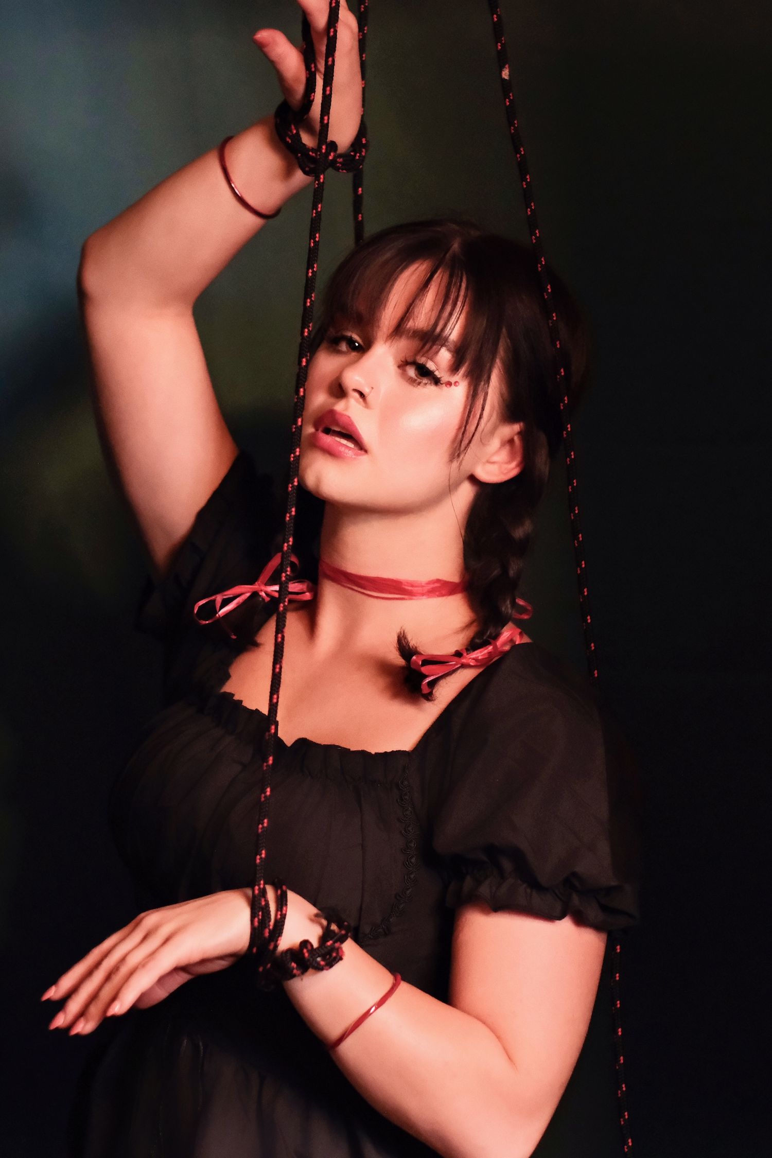 Figure in gothic black dress poses dramatically with chains in dark setting.