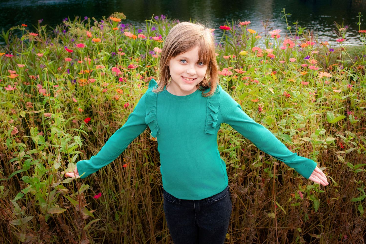 A person wearing a teal sweater spins joyfully in a garden filled with vibrant red wildflowers on a sunny day.