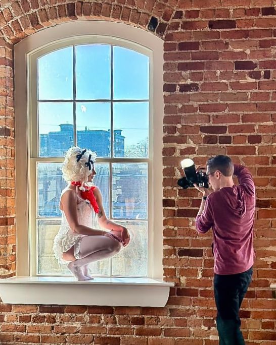 Photography session in a brick loft studio with arched window overlooking city skyline.