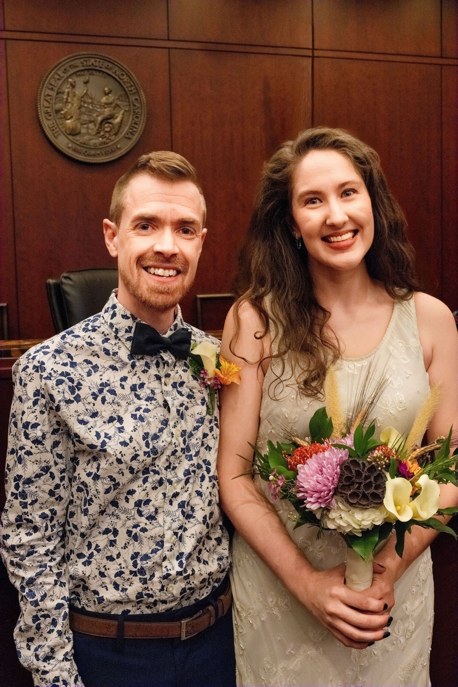 A couple poses in formal attire at a courthouse, with the bride holding a bouquet of mixed flowers.