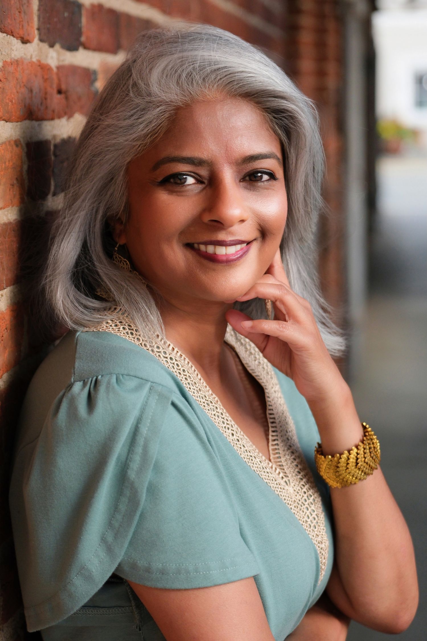 Elegant portrait against brick wall featuring mint green top and statement jewelry.