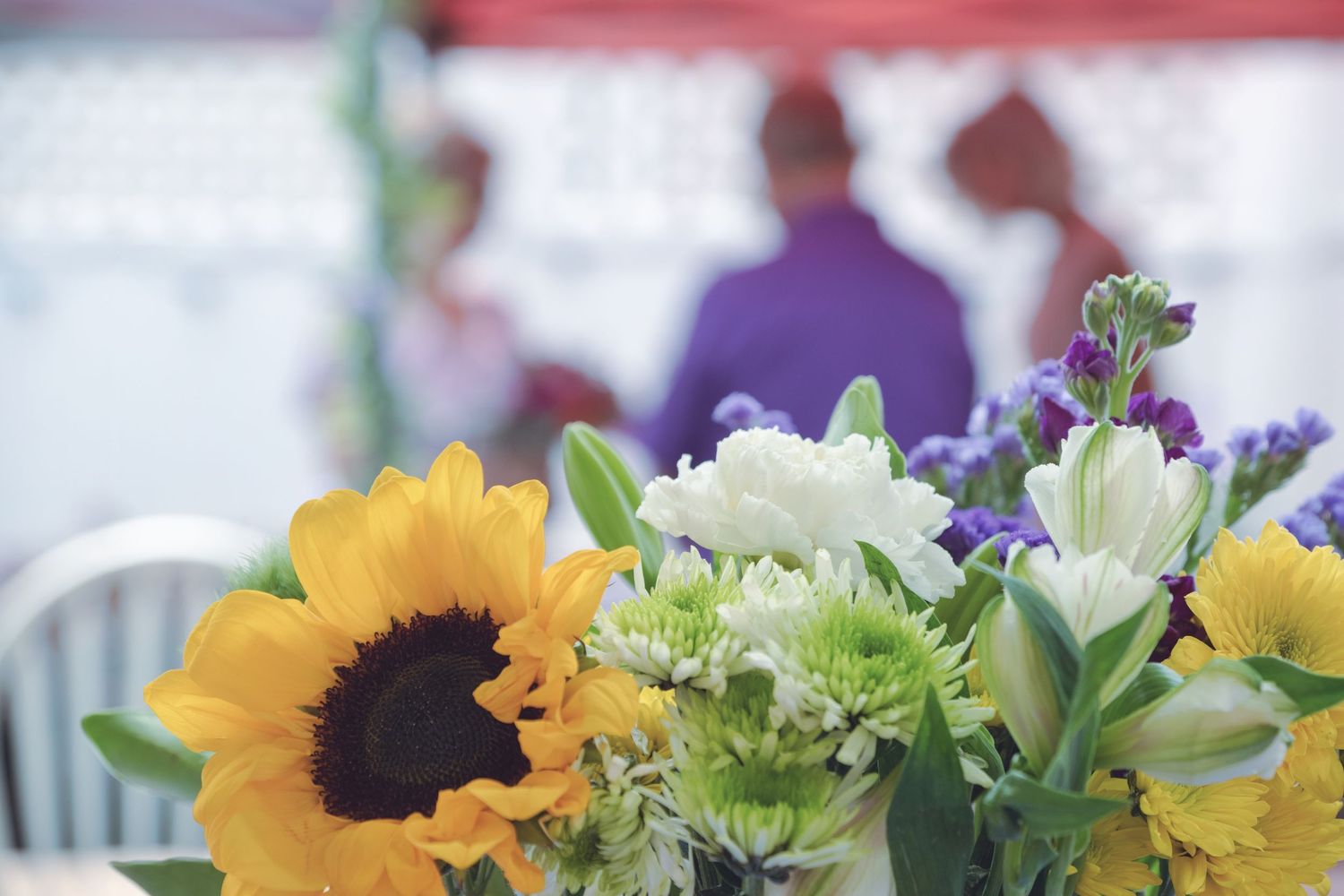 Bright sunflowers and white flowers in a bouquet arrangement with blurred background indoors.