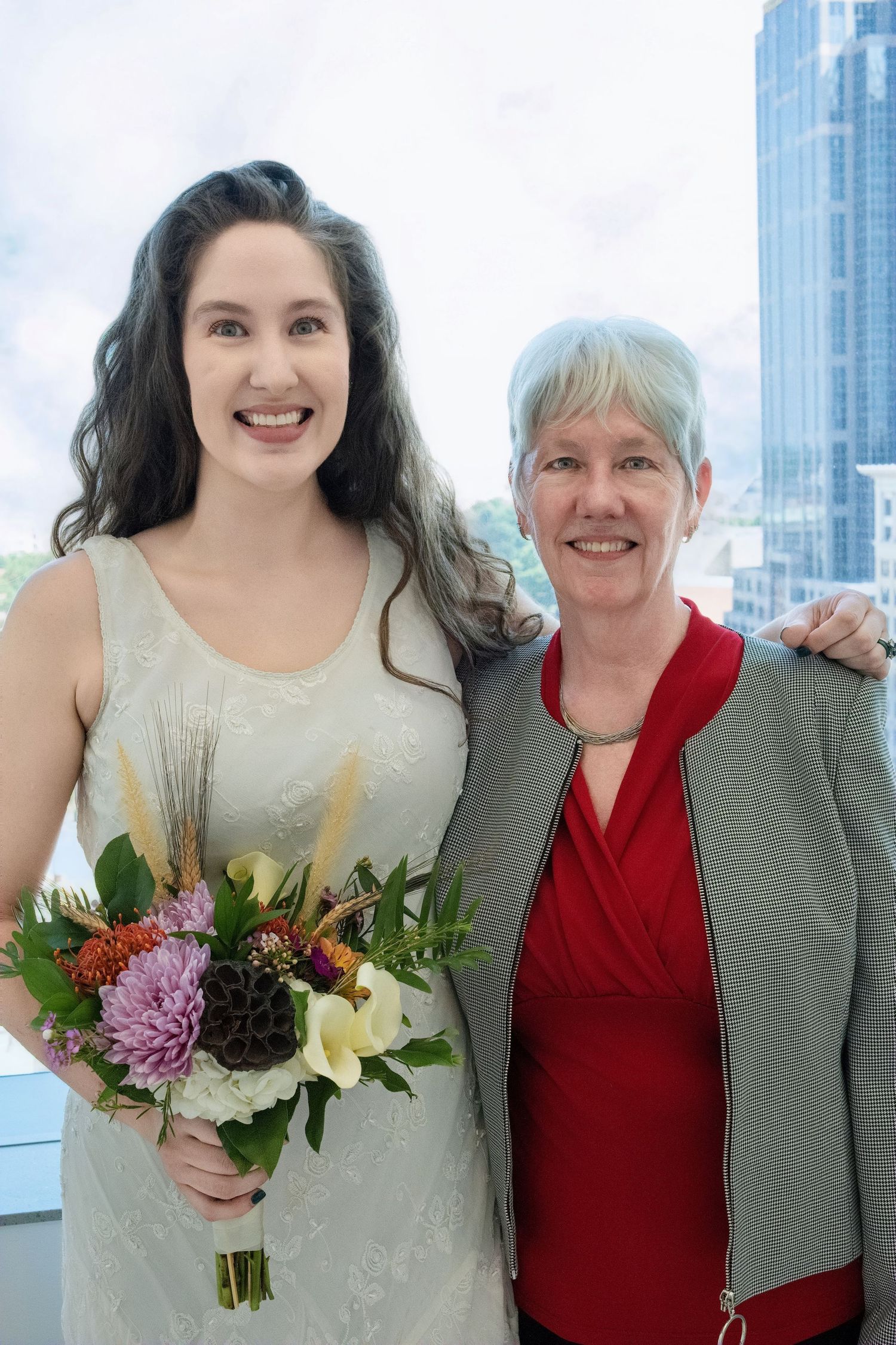 Two people posing together with a colorful bouquet of flowers against a cityscape background with tall buildings.