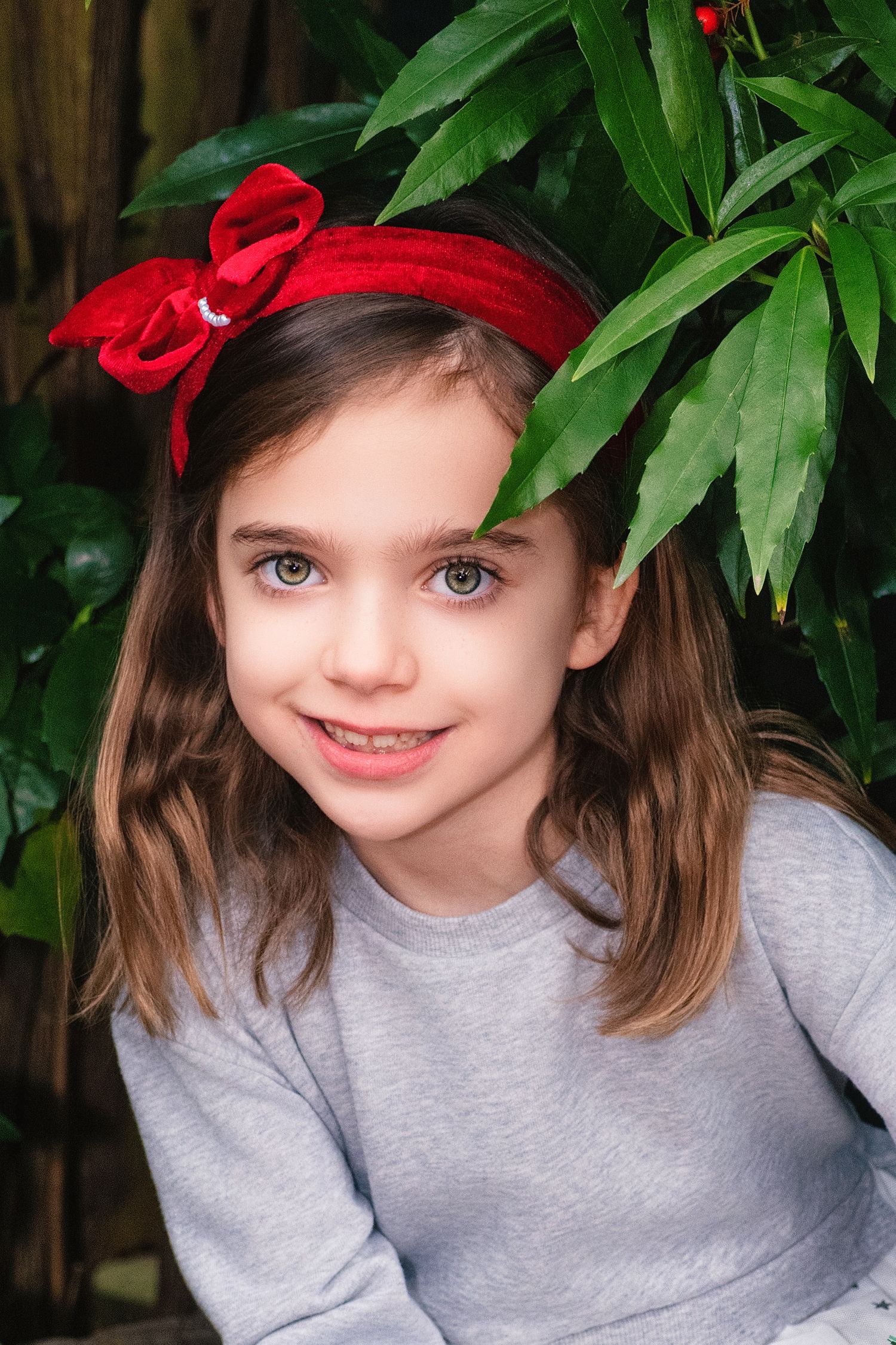 A sequence of close-up shots showing someone wearing a gray sweater and red bow against green foliage background.