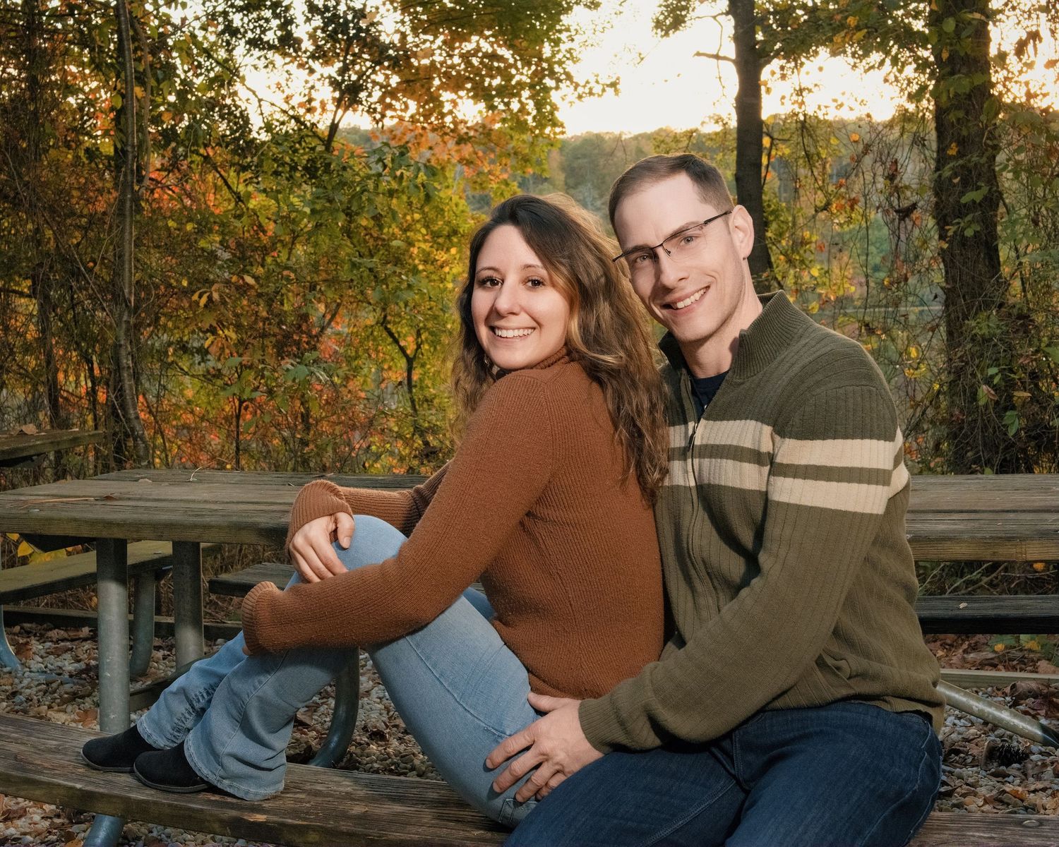 A couple sits together on wooden steps surrounded by fall foliage.