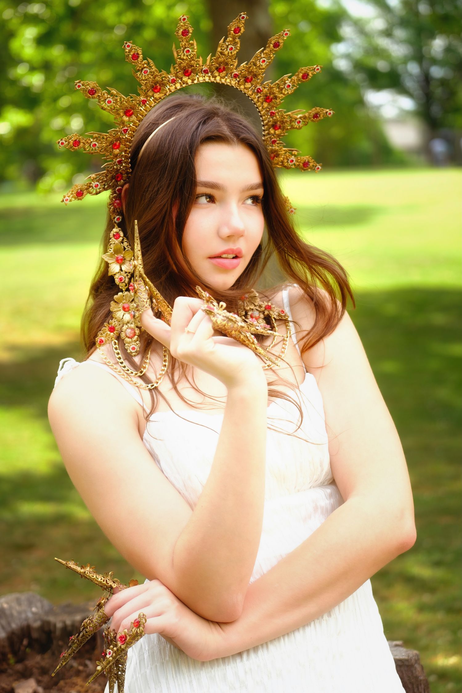 Person wearing ornate golden sun crown poses in white dress outdoors.